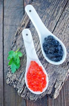 red and black caviar in white spoon and on a table