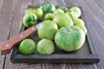 green tomato and knife on wooden board
