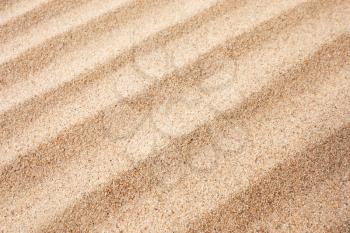 Yellow dry sand surface with grooves and wavy lines close-up diagonal view with shallow depth of field nature background