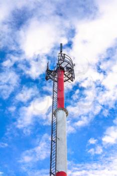 Cellular communications tower against the blue cloudy sky