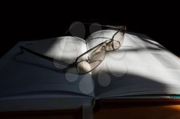 Glasses and diary on a dark background in the sunlight