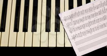 Black white keyboards with music sheet and penl close up