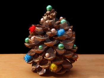 Pine cone with decorations on a dark background and a wooden surface close-up