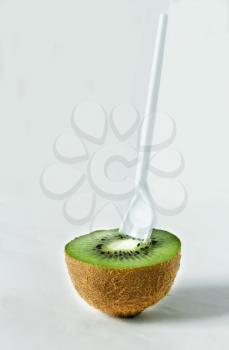 Half kiwi with a spoon on a light background