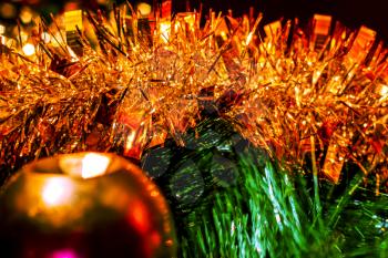 Tinsel and ball on the Christmas tree in the light of a garland