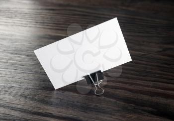 Photo of blank white business card in paper clip on dark wooden background. Blank template for branding identity. For graphic designers portfolios.