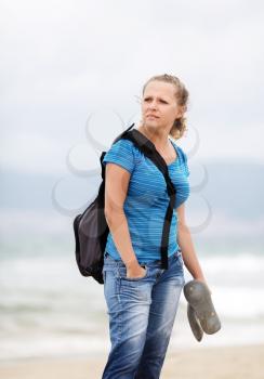 Pretty young serious blonde woman with a backpack outdoors. Girl with backpack. Selective focus on model. Vertical shot.