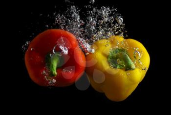 Red and yellow peppers in water with air bubbles. Photo on black background.
