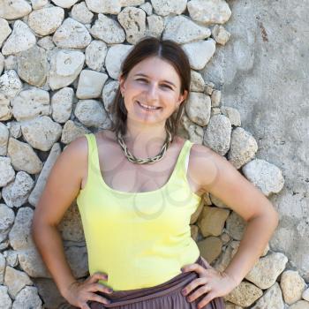 Pretty young smiling woman in a bright light green T-shirt. Old stone wall in the background.