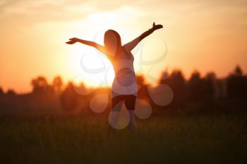 Girl with arms raised looking at the sun. Focus on model. Shallow depth of field.