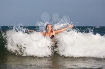 Smiling beautiful young woman in foam and spray of sea wave on a clear sunny day.
