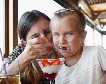 Mother feeds his daughter delicious sweet ice cream with strawberries in a restaurant. Shallow depth of field. Focus on the child's face.