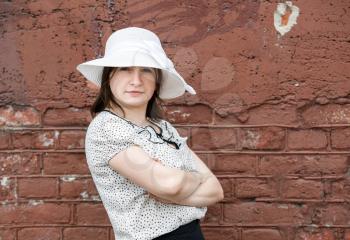 Female portrait in a retro style. Young woman in a white blouse and hat posing on a background old vintage brown brick wall.
