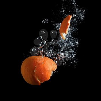 Tangerine and peel away, falling into the water with air bubbles on a black background.