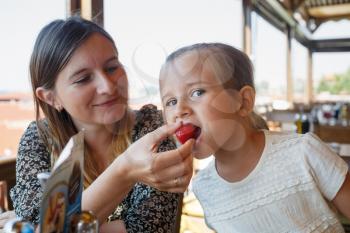 Mum feeds the child delicious sweet strawberries in the restaurant. Shallow depth of field. Focus on the child's face.