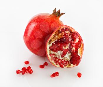 Delicious juicy ripe pomegranate and its half with reflection on a light background. Studio shot.