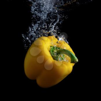 Delicious yellow sweet pepper in water with air bubbles. Photo on black background.