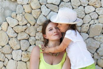 Little daughter hugging her mother. Family portrait. Smiling young woman and child on the background of an old stone wall.