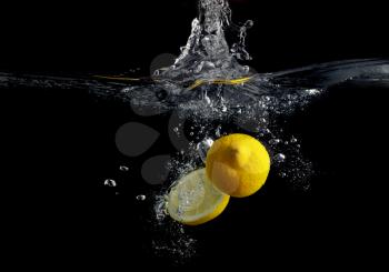 Lemon falling into the water with a splash of water and air bubbles. On a black background. Wash fruits.