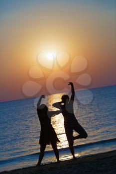 Two girls dancing at sunset on a background of the sea. Focus on models. Shallow depth of field. Toned image.