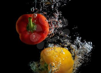 Red and yellow peppers, falling into the water with air bubbles. Photo on black background.