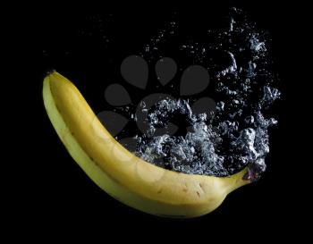Banana dropped into water on black background. Air bubbles in water.