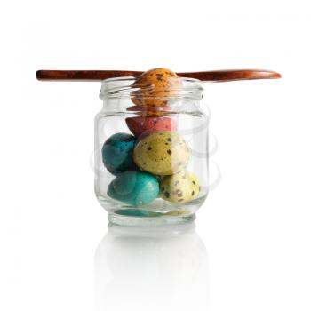 Multicolored painted quail eggs in a glass jar with a wooden spoon on a white background. Isolated with clipping path.