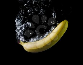 Banana dropped into water on black background. Air bubbles in water. Wash fruits.