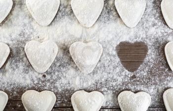 Cooking dumplings. Raw ravioli in the shape of hearts, sprinkle with flour, on wooden background closeup. Top view.