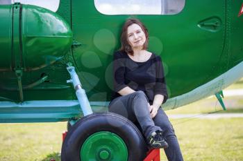 A woman posing while sitting on the wheel of a green helicopter.
