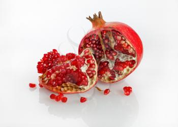 Pomegranate and its half with reflection on a light background. Studio shot.