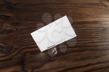 Blank business card and paper clip on dark brown wooden background. Blank template for branding identity. Mock-up for design presentations and portfolios.