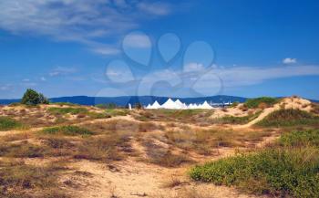 Summer sunny day. Blue sky and dry plants on the sand. White tents and mountains in the background. Black Sea coast.