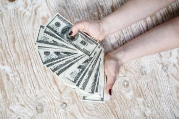 Dollar banknotes in hands. Woman hands counting dollar banknotes on light wooden background.