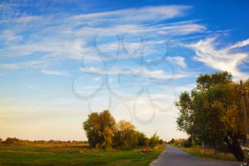 Scenic rural landscape. Old asphalt road in the countryside. Picturesque evening blue sky with clouds. Selective focus.