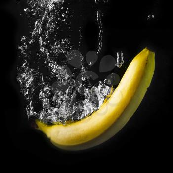 Yellow banana falling into the water with splashes and bubbles. Healthy food on black background. Wash fruits.