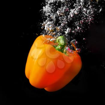 Fresh orange paprika falling into the water with a splash and air bubbles. Healthy food on black background. Wash vegetables.