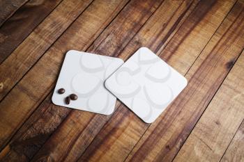 Two blank white square  coasters and coffee beans on wooden table background.