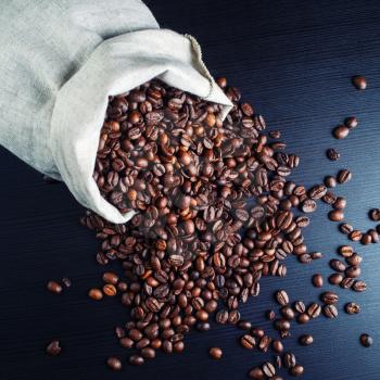 Photo of coffee beans scattered from a canvas bag on dark background.