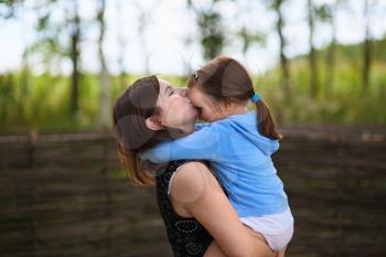 A mother's love. Mom keeps little daughter in her arms and kisses her on the forehead. Selective on the faces of the models.