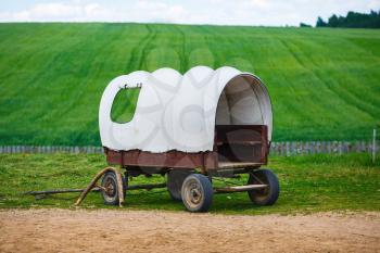 Old covered wagon with white top against green grass field background.