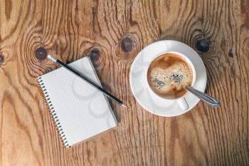 Blank notepad, pencil and coffee cup on vintage wooden table background. Template for placing your design