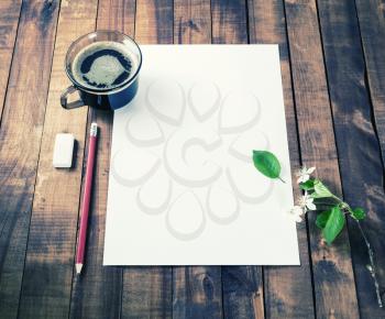 Blank sheet of paper, coffee cup, pencil, eraser, cherry flowers and green leaves on vintage wood background. Stationery template for placing your design.