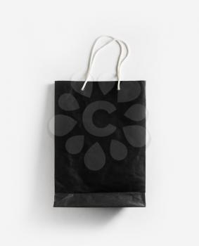 Mockup of black blank paper shopping bag with rope handles on white paper background. Flat lay.