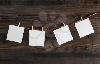 Four blank photo paper attach to rope with clothespins on wooden background.