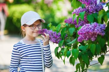 Smiling baby girl and lilac bush in the garden. Selective focus.