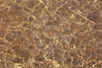 Clear sea water and sandy bottom background. Sand through the transparent water texture.
