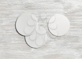 Blank white beer coasters on light wood table background. Flat lay.