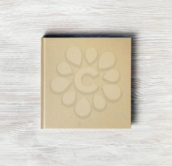 Blank square cover book on light wooden background. Responsive design template. Flat lay.