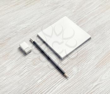 Blank square notebook, pencil and eraser on light wood table background. Responsive design mockup.
